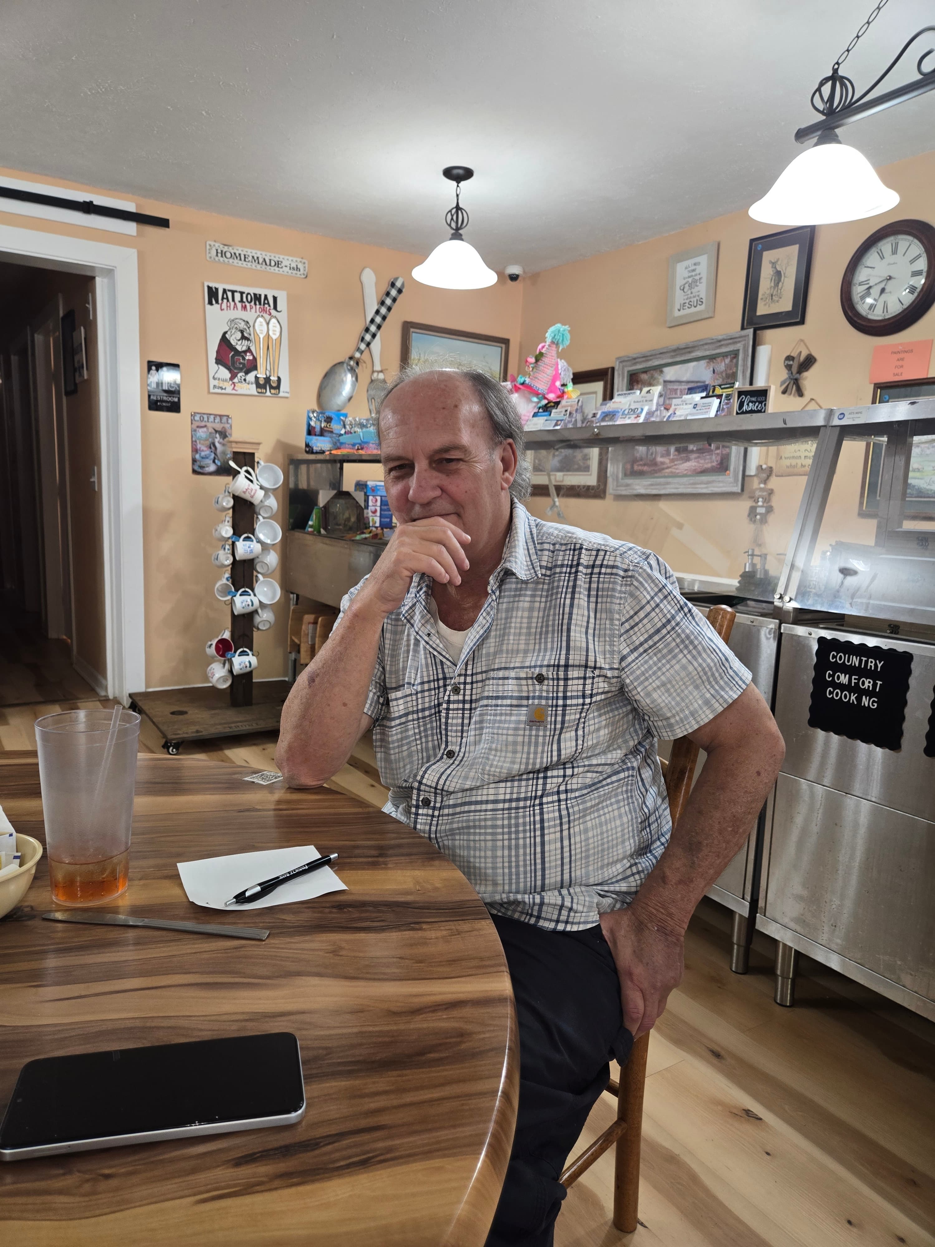 Man in a plaid shirt sits at a wooden table in a cozy country cafe.