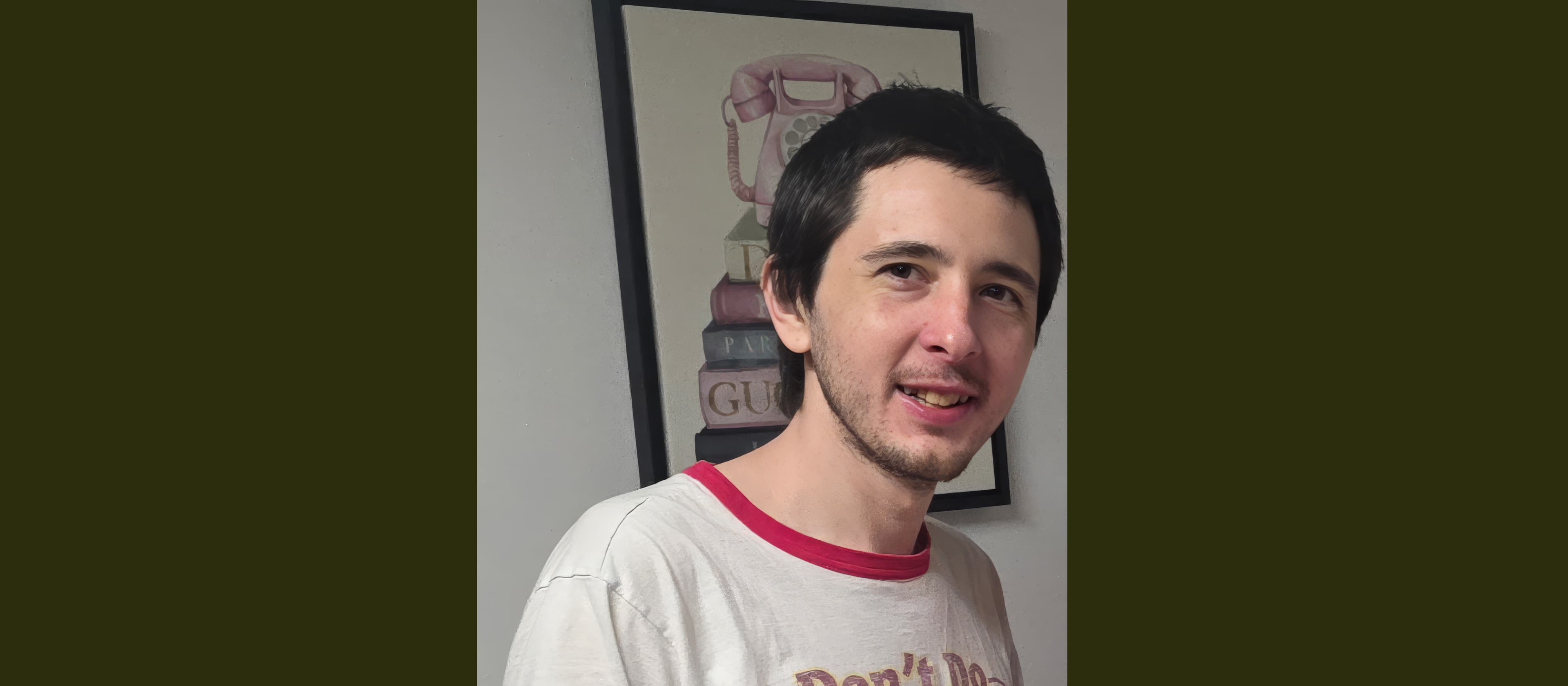 Smiling man with dark hair and beard in front of a pink telephone painting.