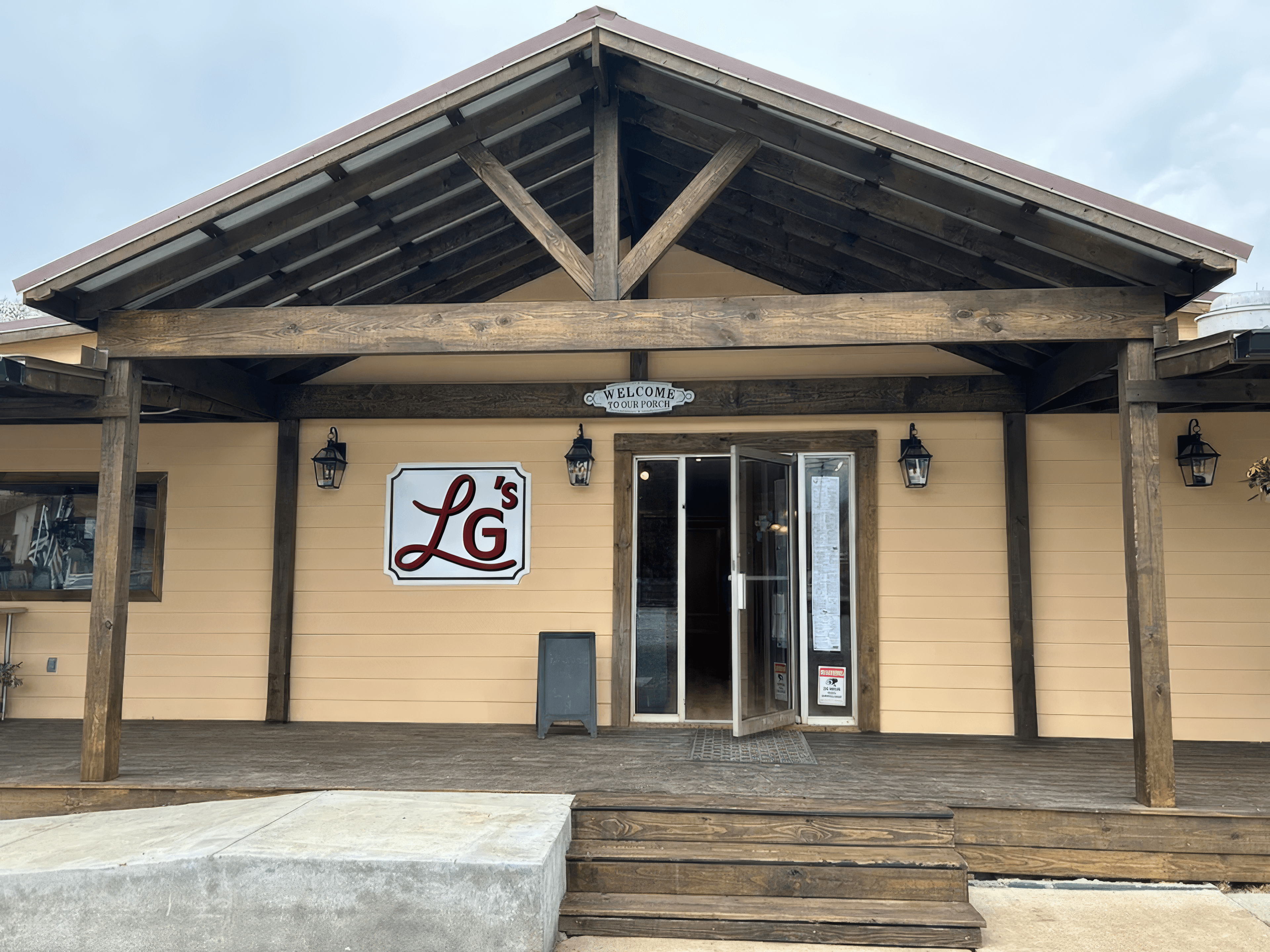 Tan building with a wooden porch, gabled roof, and a red LG's sign.