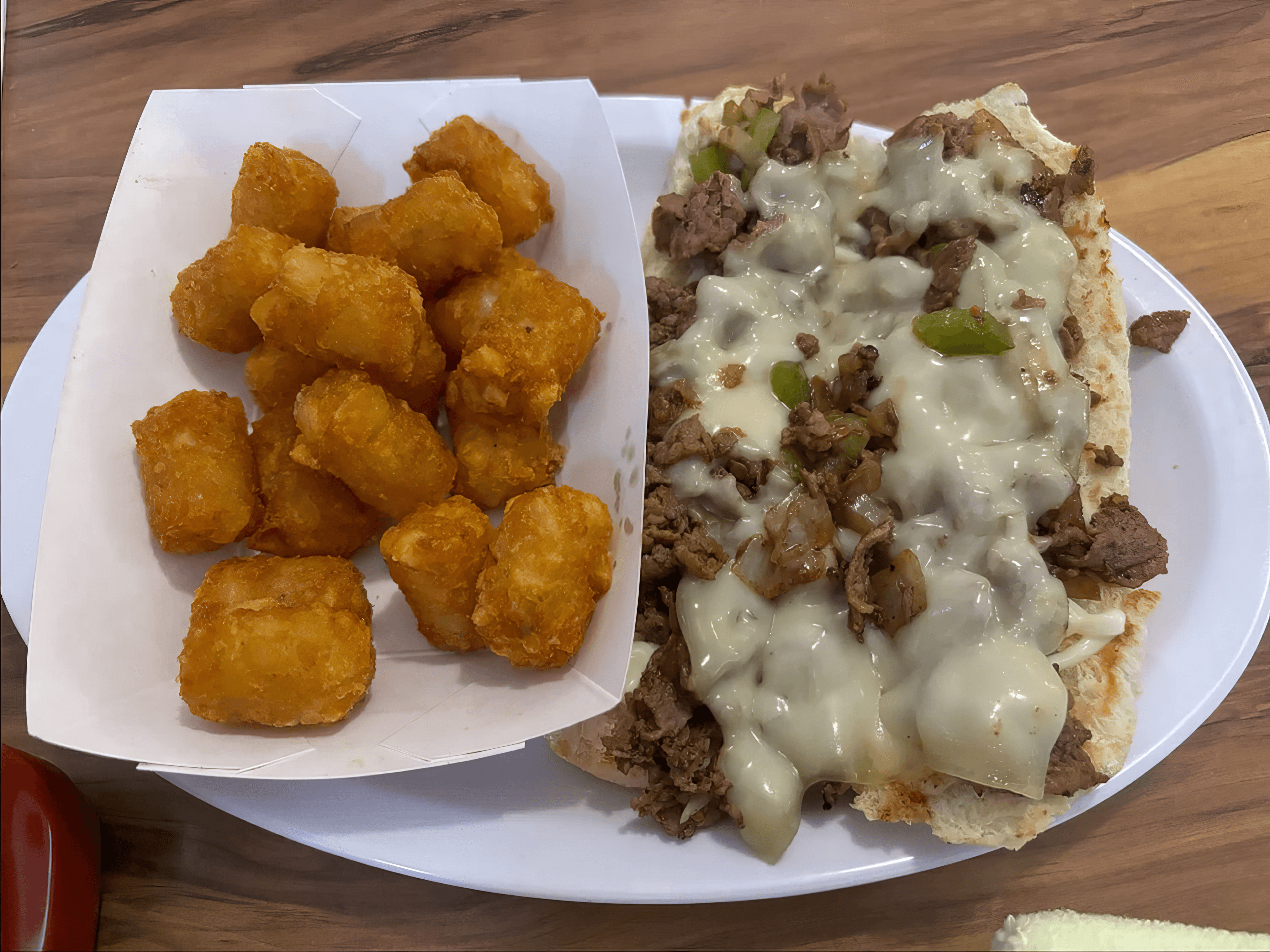 Philly cheesesteak with melted cheese and peppers alongside a tray of golden tater tots.