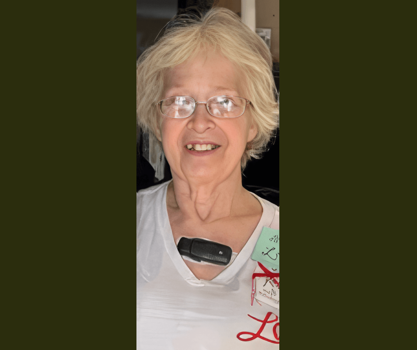 Smiling woman with blonde hair and glasses wearing a white shirt and a medical device.