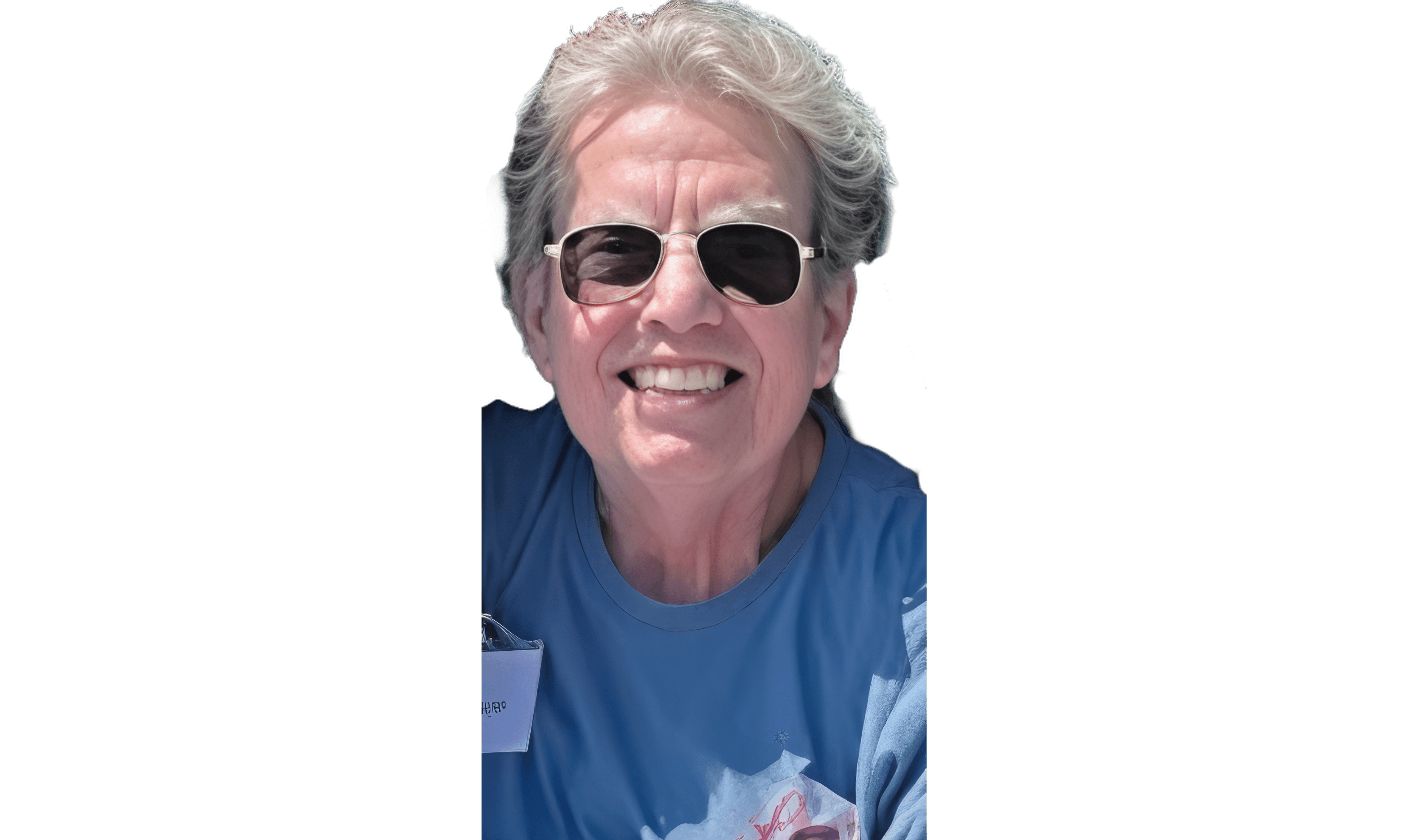 Smiling older person with short, wavy gray hair wearing sunglasses and a blue shirt.